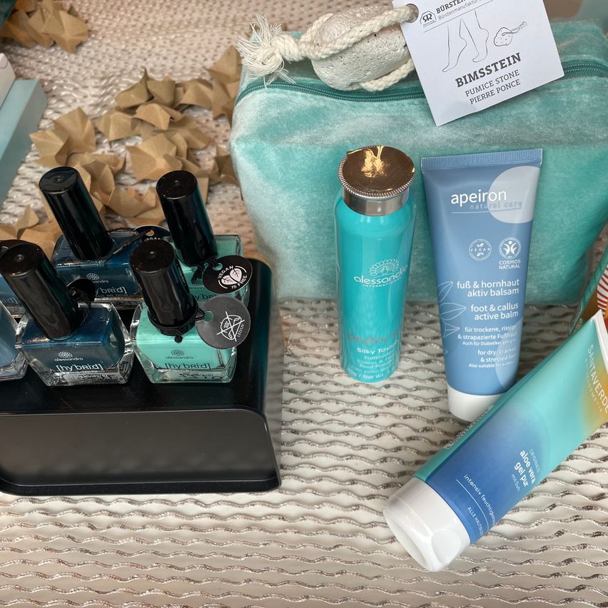 Eine Sammlung von Hautpflege- und Nagelprodukten, einschließlich einer blauen Tasche, Nagellackflaschen, einer blauen Flasche und einer Tube Creme.
