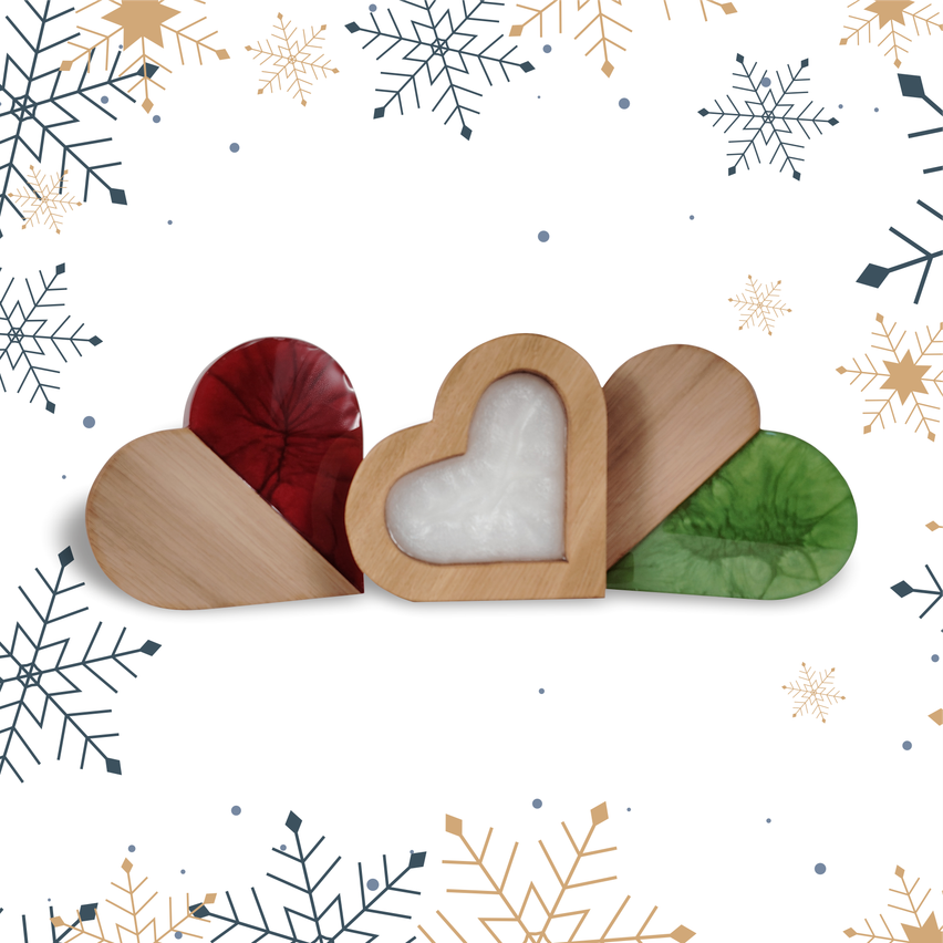 Drei holzerne herzförmige Objekte auf weißem Hintergrund mit Schneeflocken. Ein Herz ist rot, eines hat einen weißen Mittelpunkt und eines ist grün.