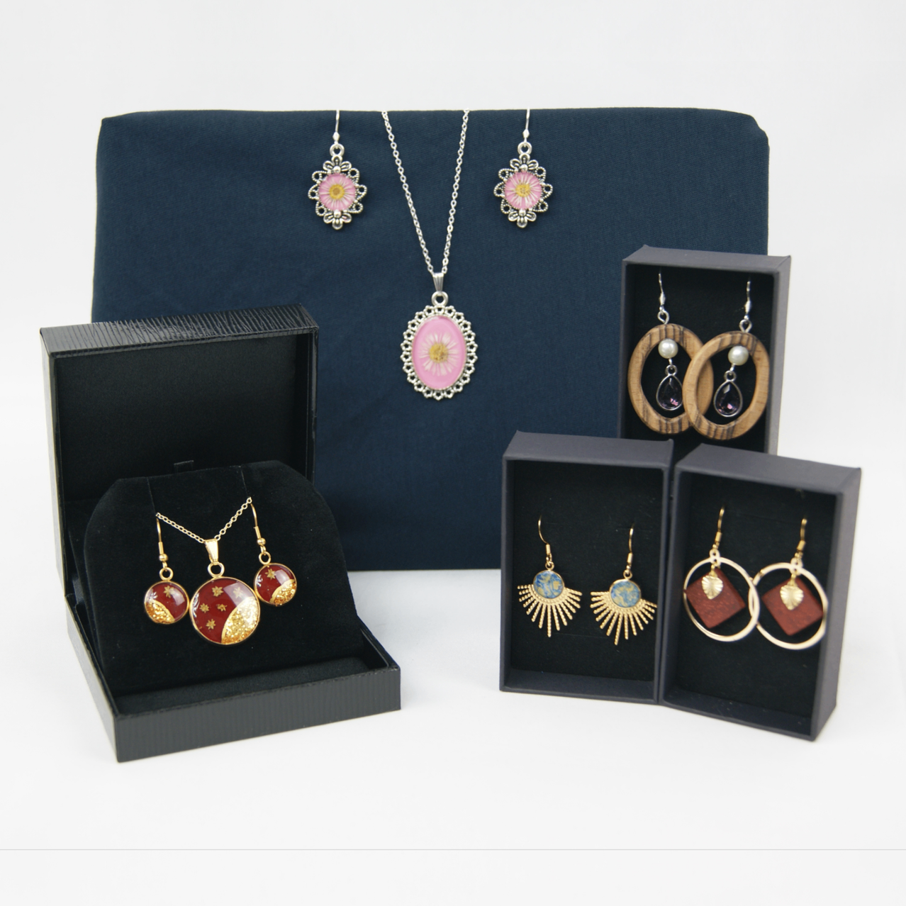 Eine Ausstellung von Schmuck in schwarzen Boxen. Eine Halskette mit Blumenanhänger, Ohrringe und ein Anhänger. Ein weiteres Set enthält Holzohrringe und einen Holzanhänger.