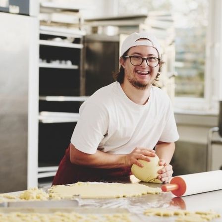 Ein Mann in der Küche arbeitet mit Teig, lächelt und hält einen Nudelholz.