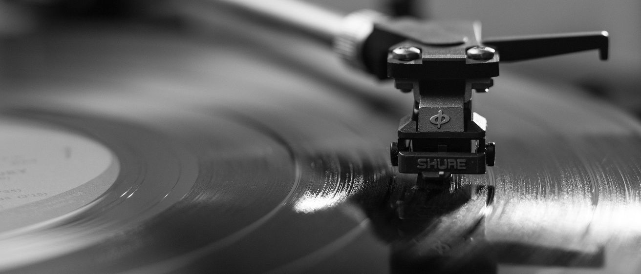 Ein schwarz-weißes Bild eines Plattenspielers mit der Nadel auf einer Schallplatte. Der Plattenspieler hat ein Shure-Logo auf der Tonabnehmernadel.