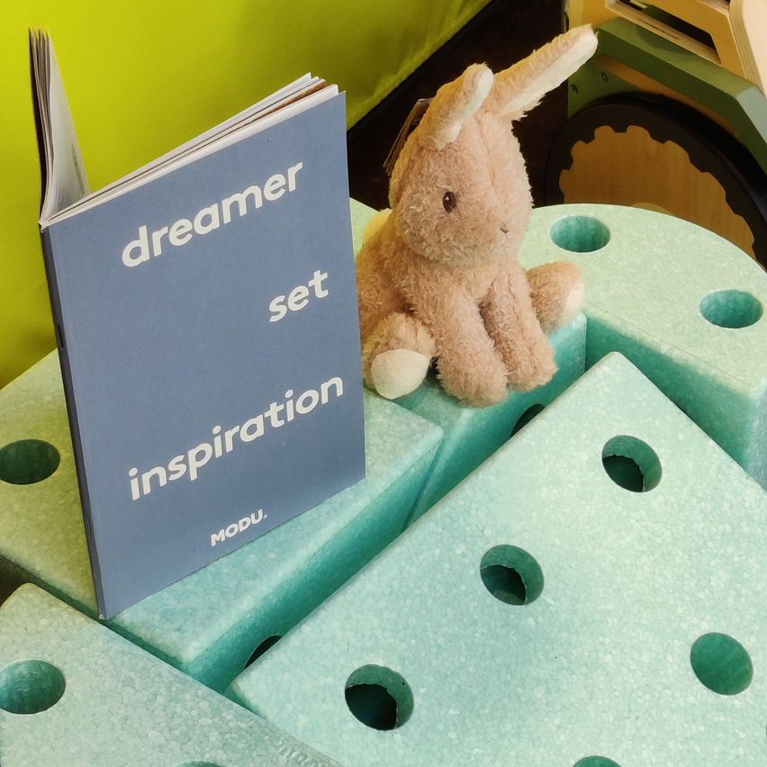 Ein Buch mit dem Titel 'Traumset Inspiration' von MODU liegt neben einem Kuscheltier auf einem Schaumstoffbrett mit Löchern.