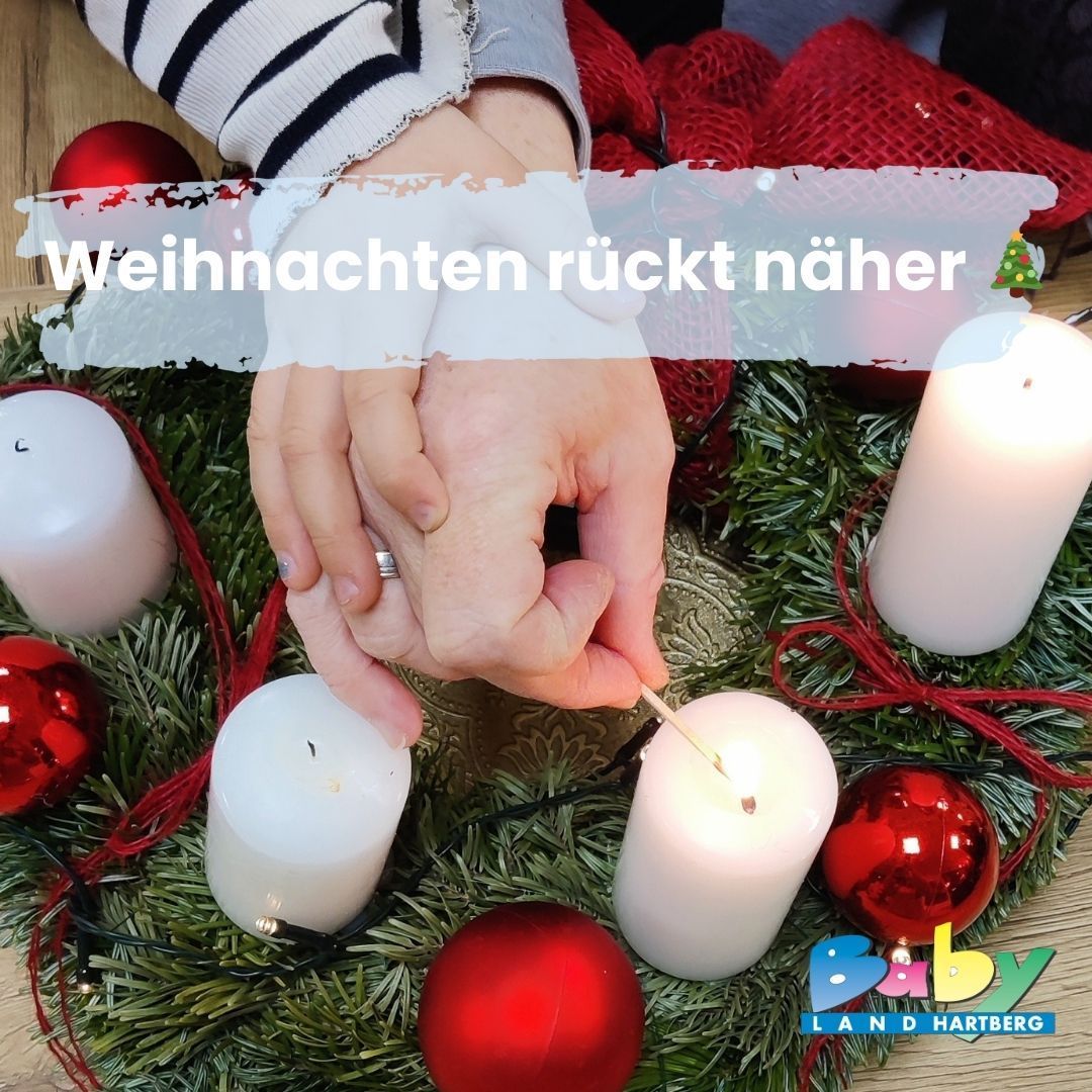 Eine Person zündet mit einem Streichholz eine Kerze in einem Kranz mit Weihnachtsdekoration an. Der Kranz hat rote Kugeln und grüne Blätter. Das Bild hat einen Wasserzeichen in der unteren rechten Ecke.