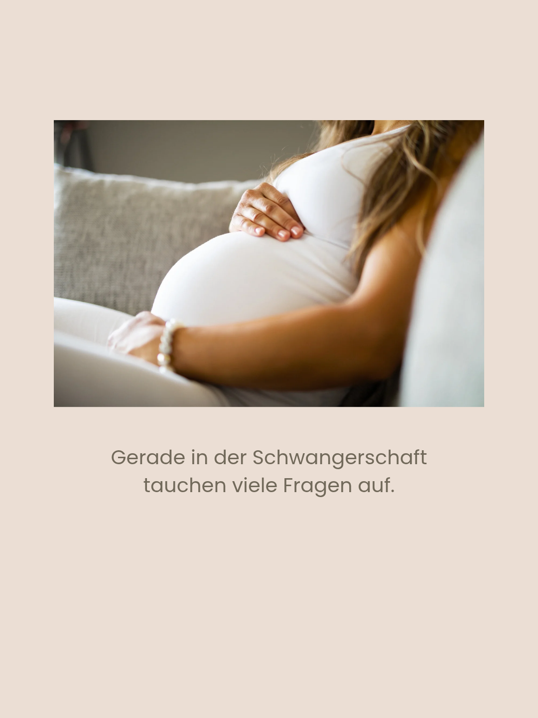 Eine schwangere Frau sitzt auf einer Couch und berührt sanft ihren Bauch. Sie trägt ein weißes Oberteil und ein Armband. Die Couch ist grau und der Hintergrund ist unscharf.
