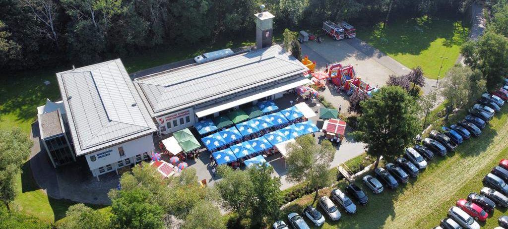 Eine Luftaufnahme eines Gemeindezentrums mit mehreren Zelten im Freien, geparkten Autos auf einem Parkplatz und einem Feuerwehrauto in der Nähe.