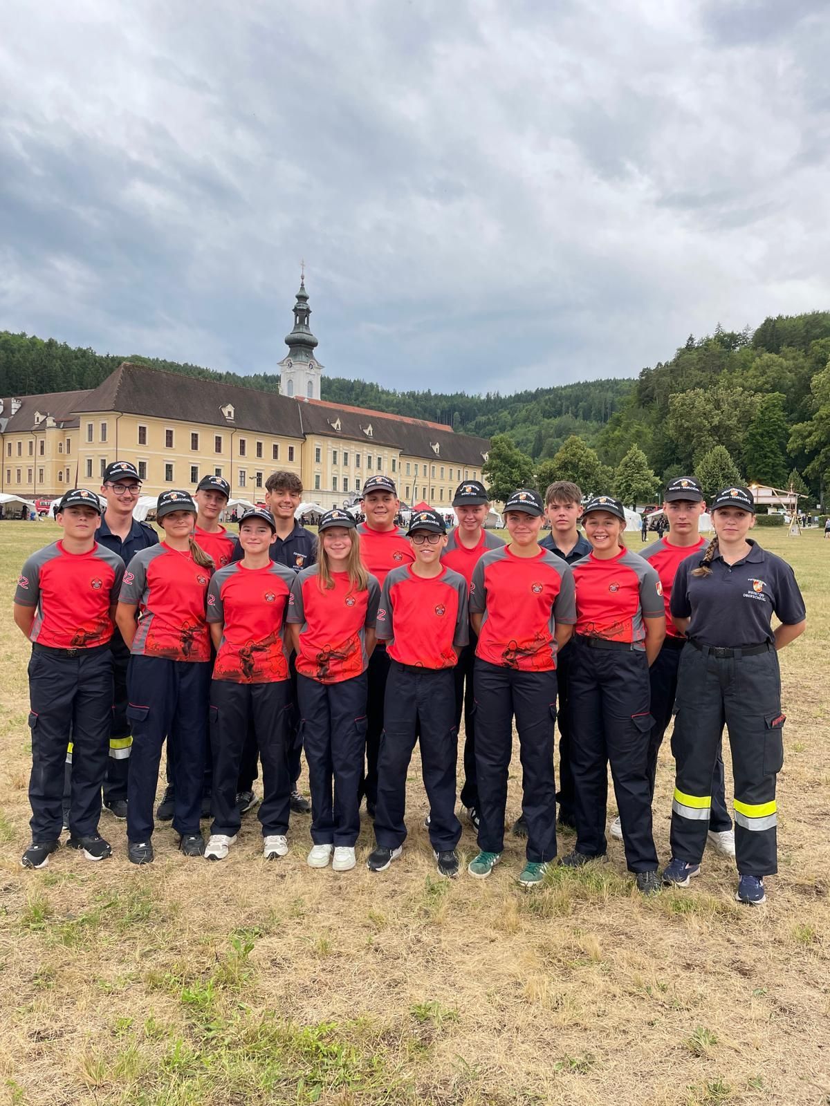 Eine Gruppe junger Menschen in roten und grauen Uniformen posiert für ein Foto vor einem historischen Gebäude mit einem Turm.