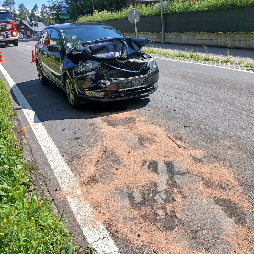 Ein schwarzer Wagen mit schweren Frontschäden steht am Straßenrand, mit Reifenspuren und Trümmern auf dem Asphalt.
