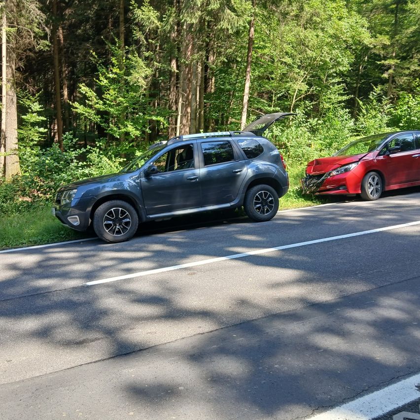 Ein grauer SUV mit offenem Kofferraum steht am Straßenrand neben einem roten Auto mit beschädigter Front.