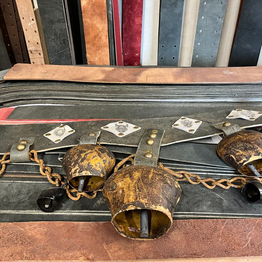 Eine Sammlung antiker Lederriemen mit goldenen Schnallen und Glockenverzierungen auf einem Tisch. Die Riemen haben einen rustikalen Look und gehören möglicherweise zu einem alten Kostüm.