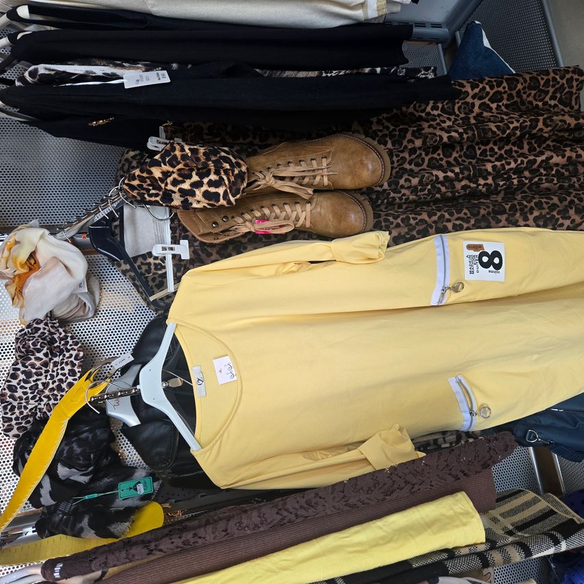 A collection of clothes and accessories on display, including a yellow shirt, brown boots, a leopard-print hat, and various other items.