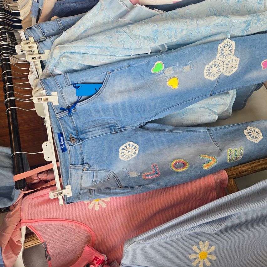 A collection of light blue jeans with decorative embroidery, some featuring the word 'love' and colorful heart motifs, displayed on a clothing rack.