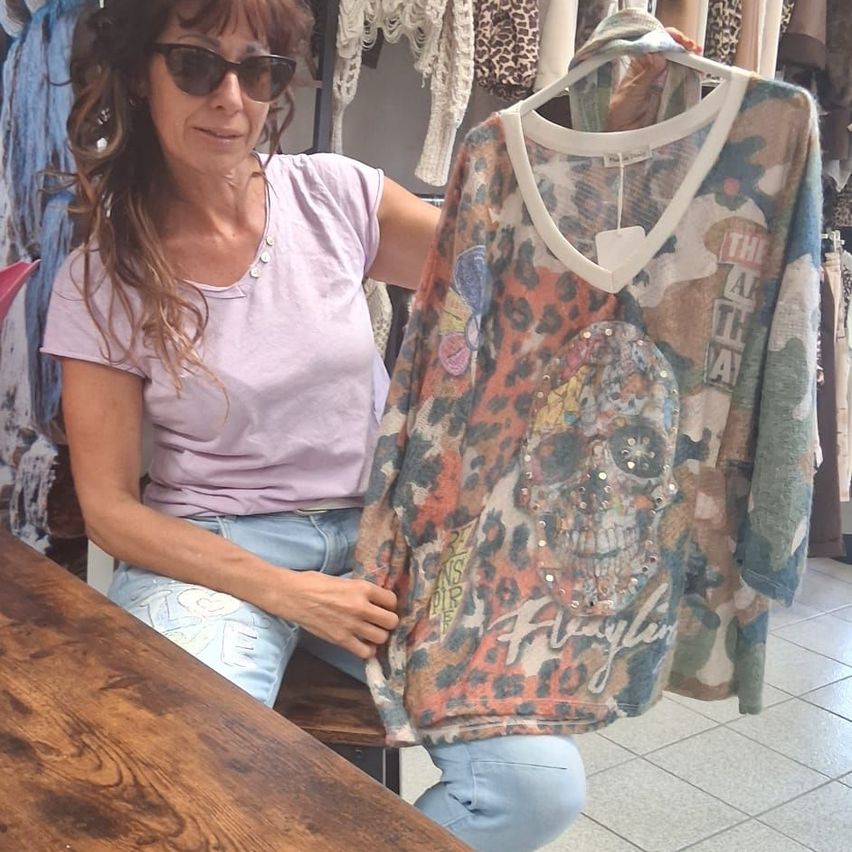 A woman wearing sunglasses and a pink shirt is holding a camouflage top with a skull design.