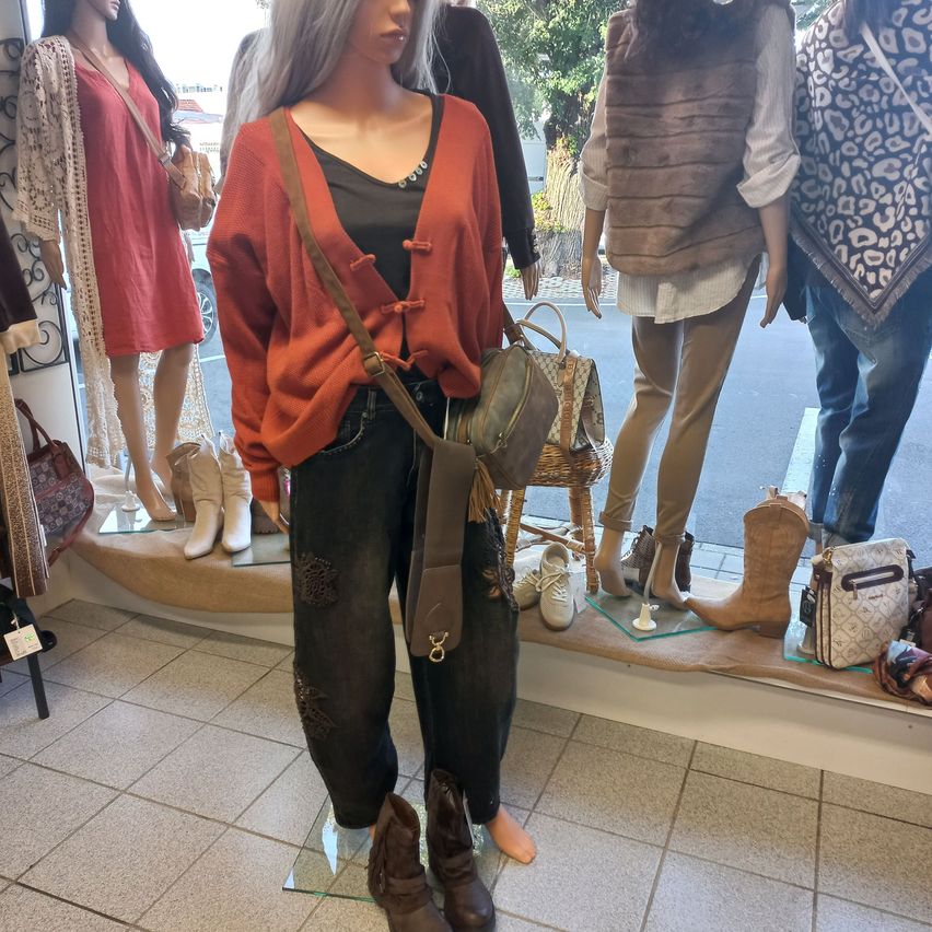 A mannequin dressed in a red cardigan, black pants, and brown boots stands in a clothing store display.