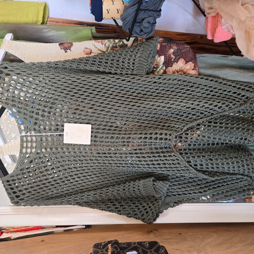 Ein grünes gestricktes Oberteil mit einem Etikett ist auf einer weißen Oberfläche neben verschiedenen Stoffen ausgestellt.
