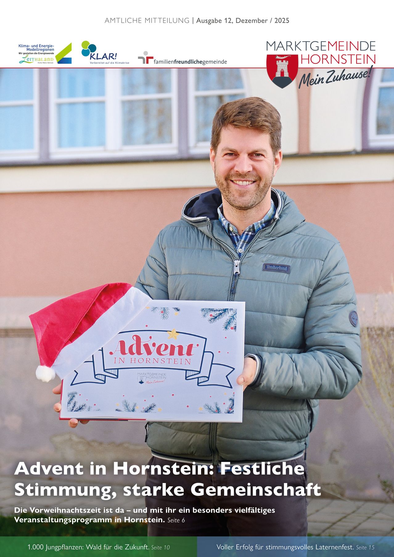 Ein Mann in einer grauen Jacke und einem karierten Hemd lächelt, während er eine Schachtel mit Weihnachtsthema hält. Er steht vor einem Gebäude mit Glasfenstern.