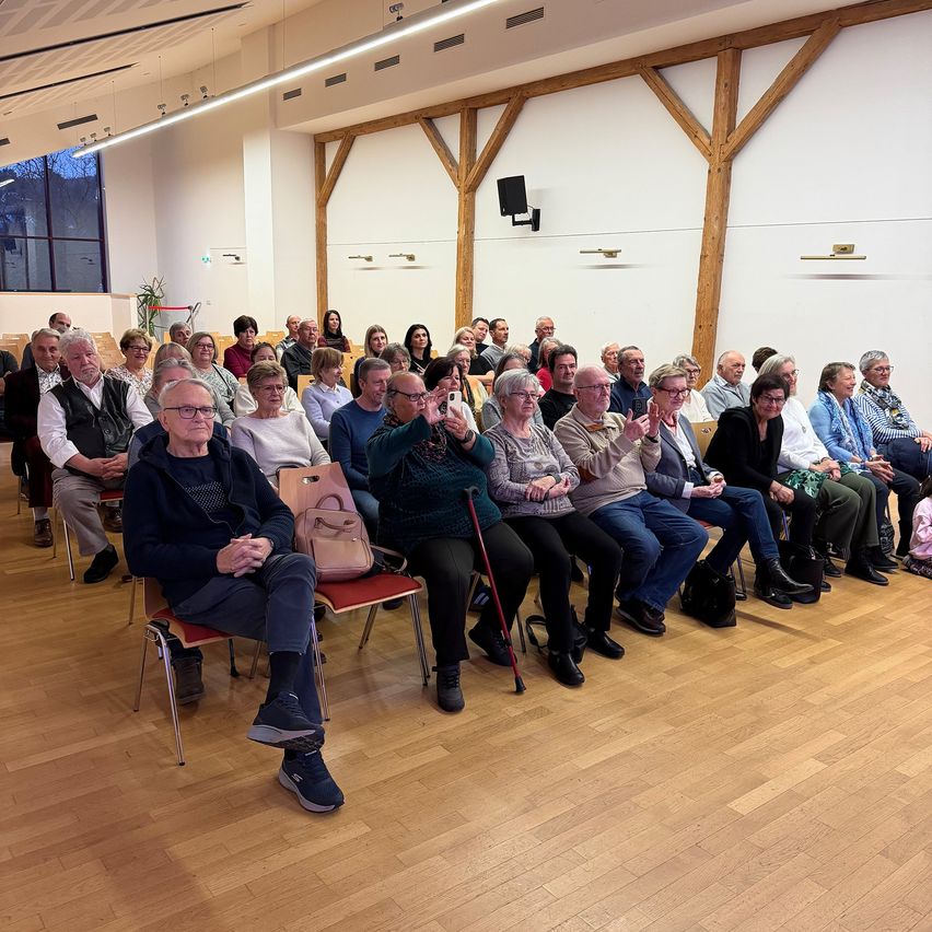 Eine Gruppe älterer Erwachsener sitzt in einem Hörsaal, der Bühne zugewandt. Einige klatschen.