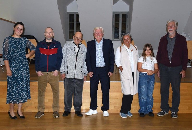 A group of people standing together, smiling and posing for a photo in a room with wooden floors and white walls.