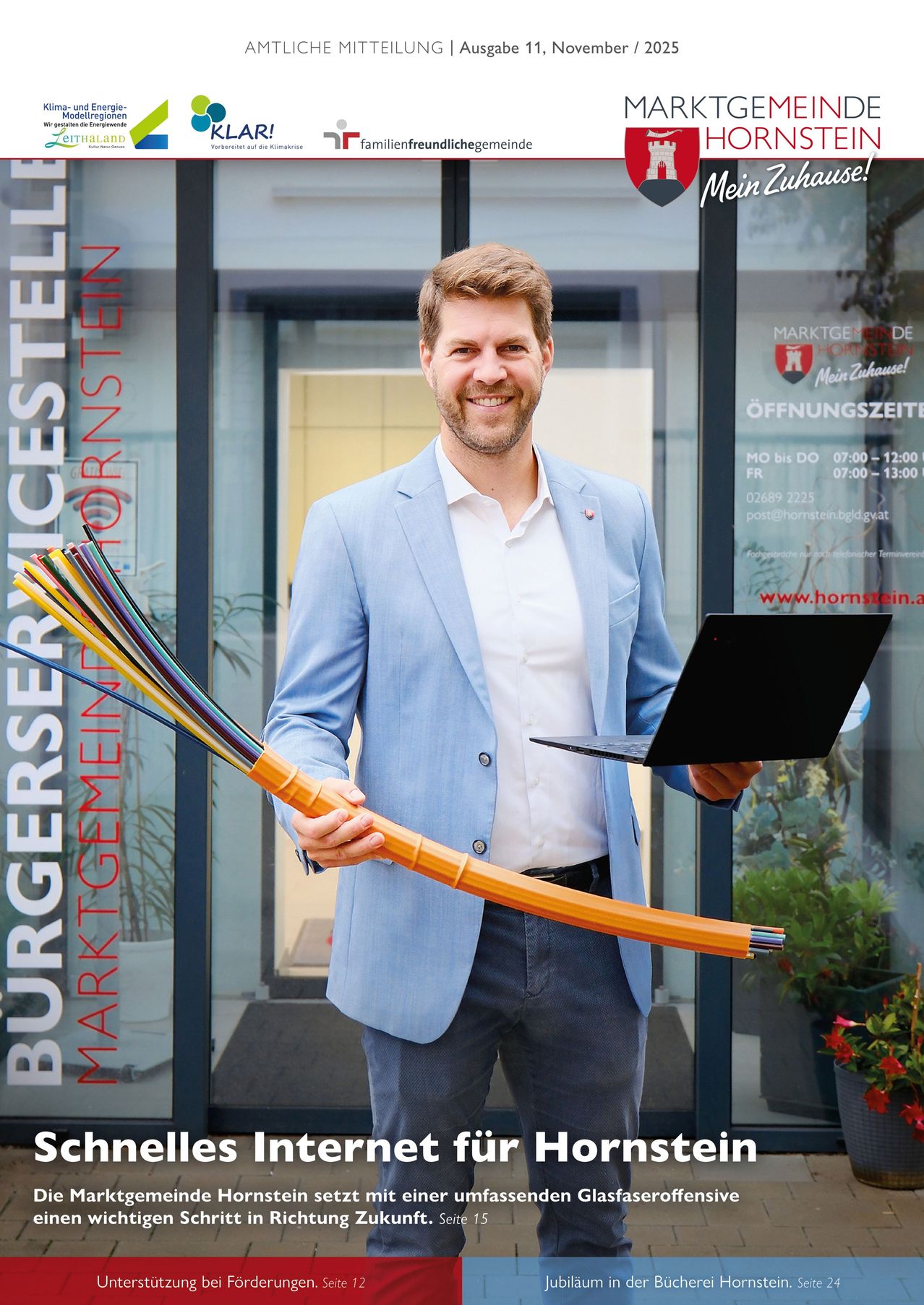A man in a blue suit is smiling while holding a laptop and a bundle of cables in front of a building.