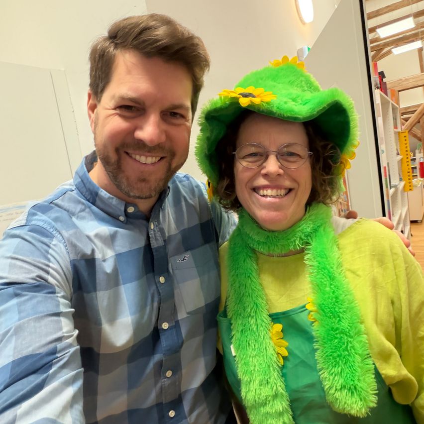 A man and a woman in a green sunflower costume smile for a photo in an indoor space.
