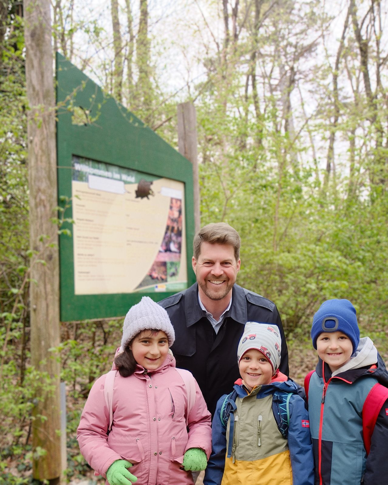 A man and three children pose for a photo in front of a green sign in a wooded area.