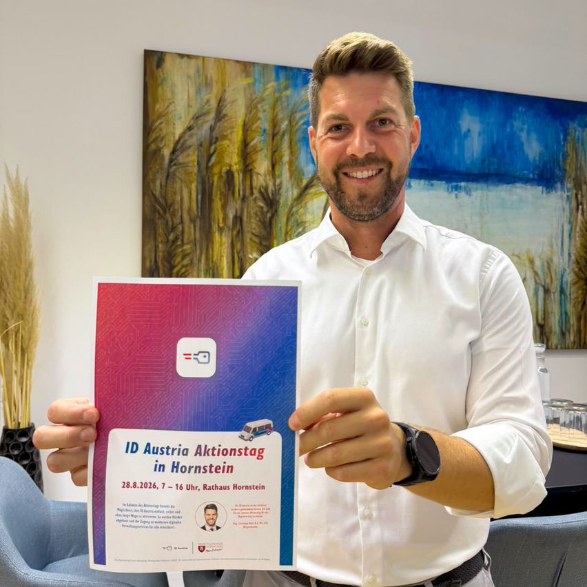 A man in a white shirt holds up a colorful flyer for the ID Austria Aktionstag in Hornstein, Austria. The flyer has a bus image and event details.