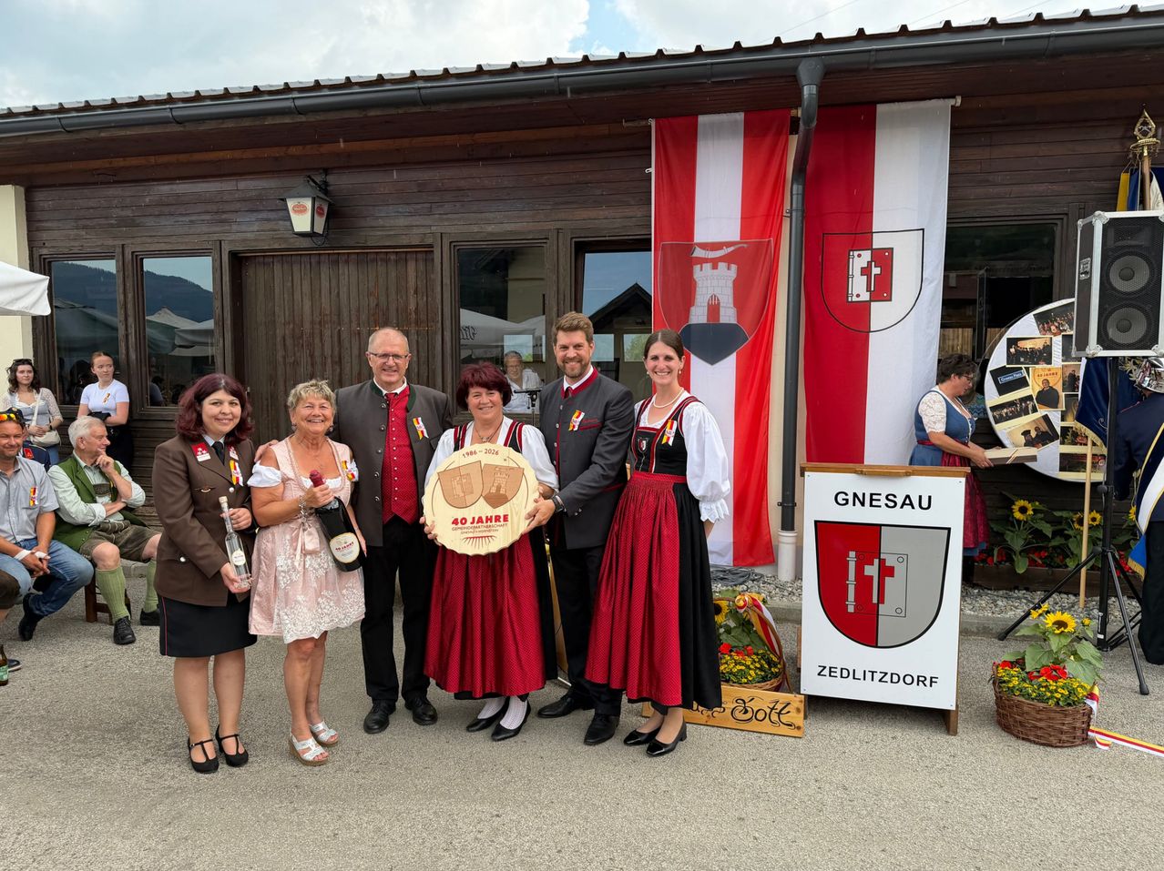 A group of adults in traditional attire holding a commemorative plaque stand in front of a building with a sign reading Gnesau Zedlitzdorf.