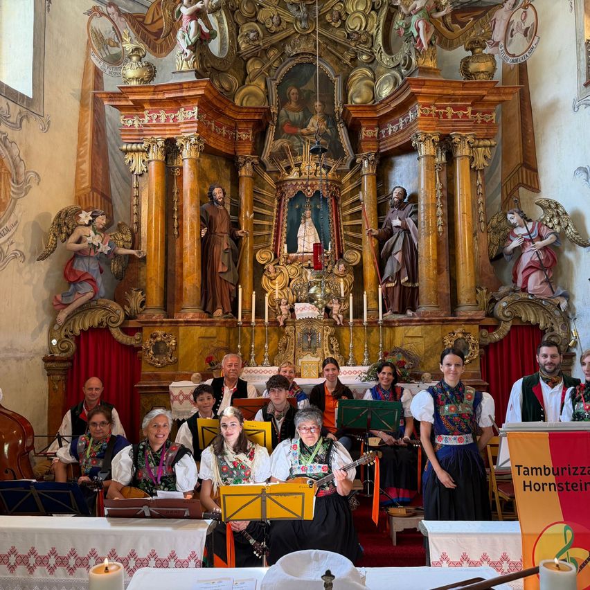 A group of musicians stands in front of an ornate church altar, adorned with statues and candles, playing traditional instruments.