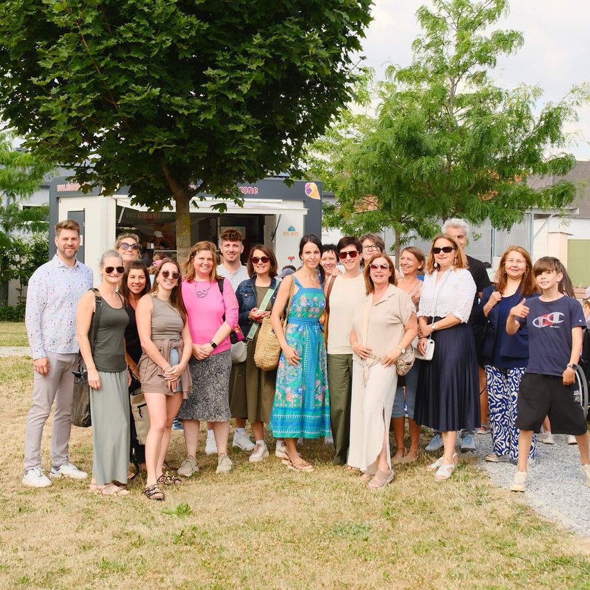 A group of people are posing for a picture in a park with trees and a building in the background.