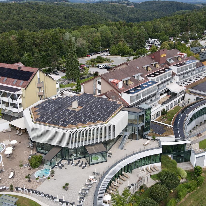 Luftaufnahme eines modernen Gebäudes mit Solarpanelen auf dem Dach und einem Swimmingpool davor.