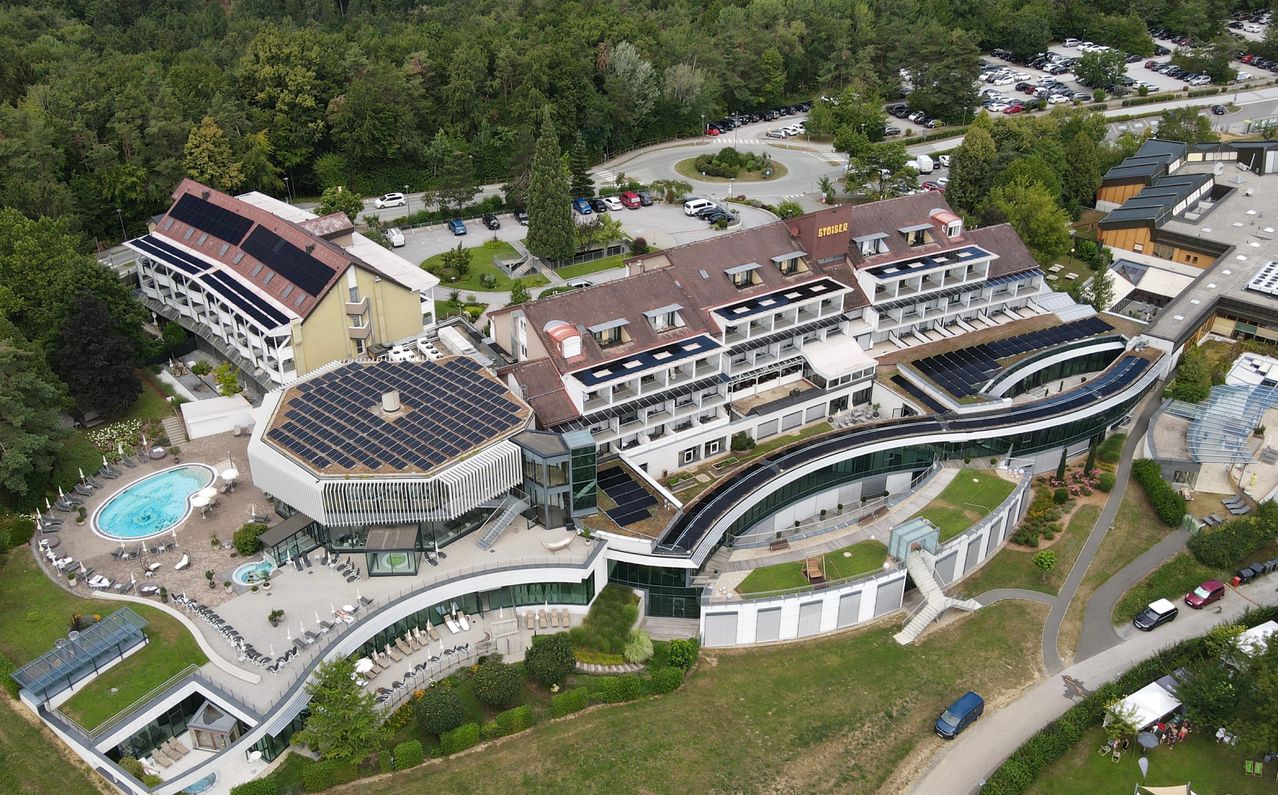 Ein Luftbild eines modernen Architekturgebäudes mit Solarpanelen auf dem Dach und einem großen Parkplatz im Hintergrund.