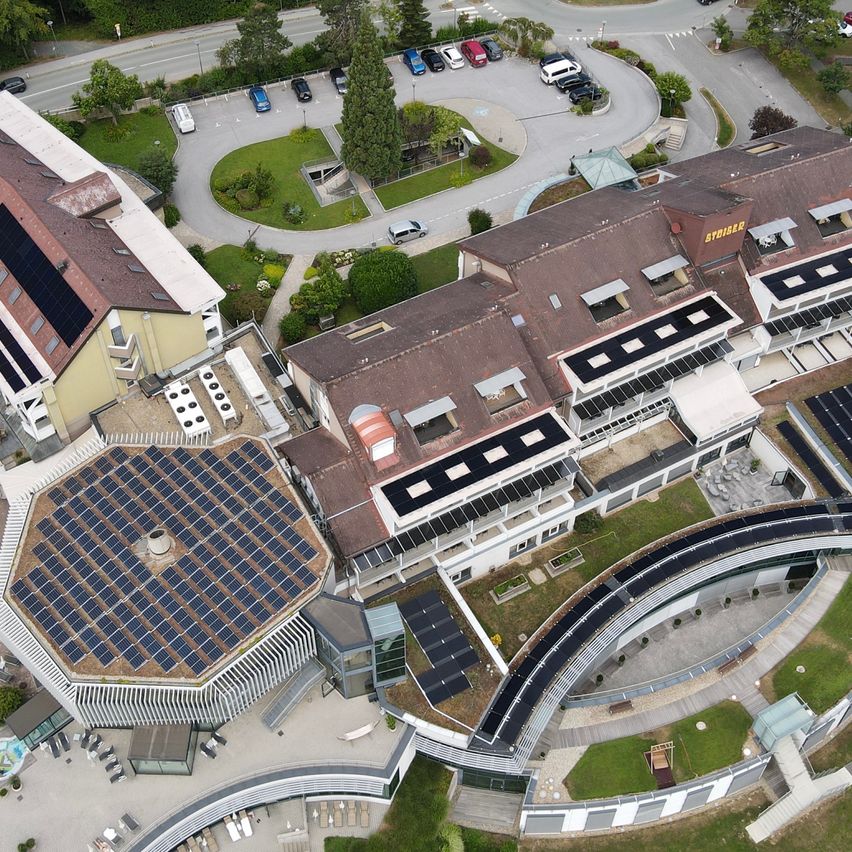 Luftaufnahme eines modernen Gebäudekomplexes mit Solarpanelen auf den Dächern und einer großen kreisförmigen Struktur im Vordergrund.