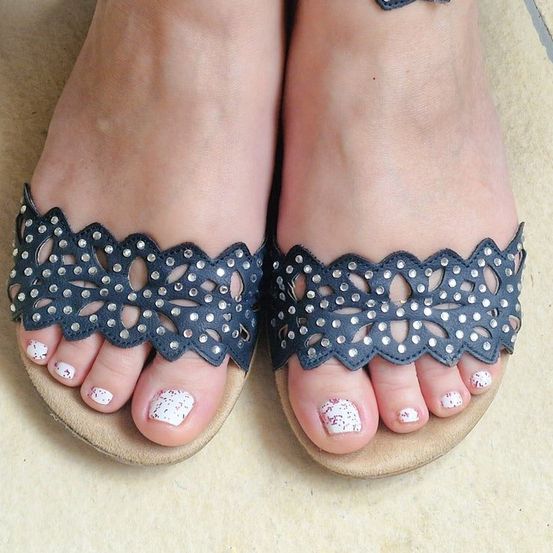 Nahaufnahme der Füße einer Person in dekorativen Sandalen mit weißem Nagellack und silbernen Details.