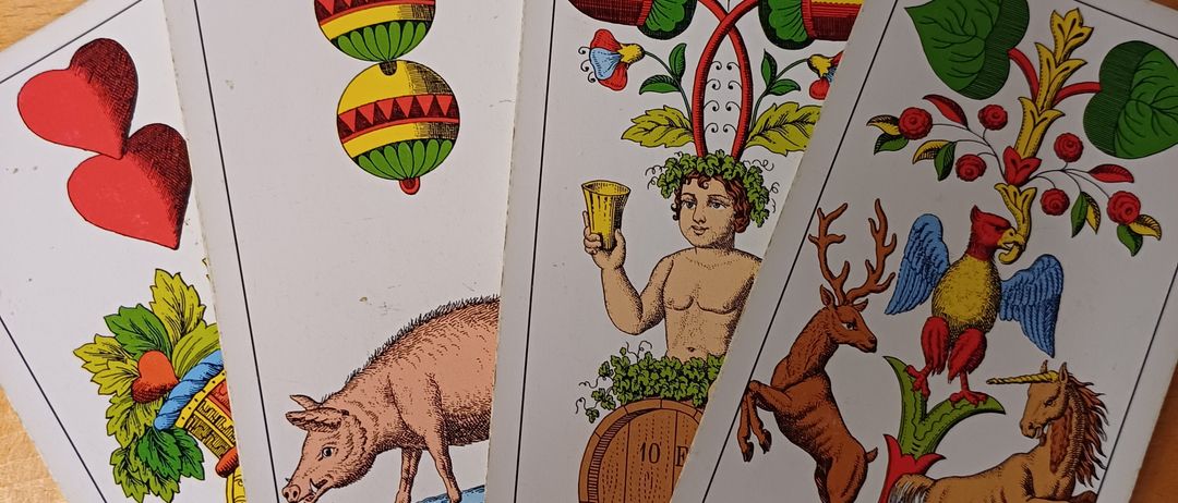 Vier Tarotkarten auf einer Holzoberfläche. Eine Karte zeigt ein Schwein, eine andere einen Mann, der einen Becher hält, während die anderen beiden Tiere und Pflanzen abbilden.