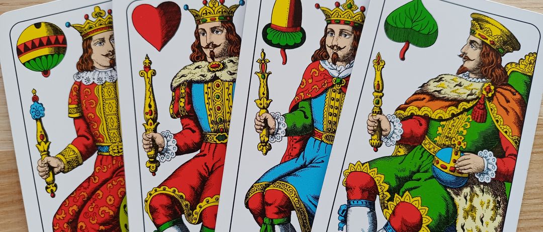 Vier Tarotkarten liegen auf einer Holzoberfläche. Jede Karte zeigt eine Figur mit Krone und Zepter. Sie sind in königliche Kleidung gehüllt.