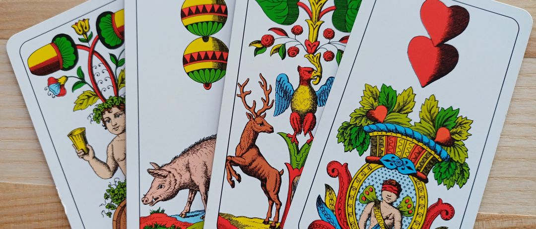 Vier Tarotkarten mit lebhaften Illustrationen: ein Schwein, ein Hirsch, ein Vogel und zwei Herzen. Jede Karte hat ein einzigartiges Design auf einer Holzoberfläche.