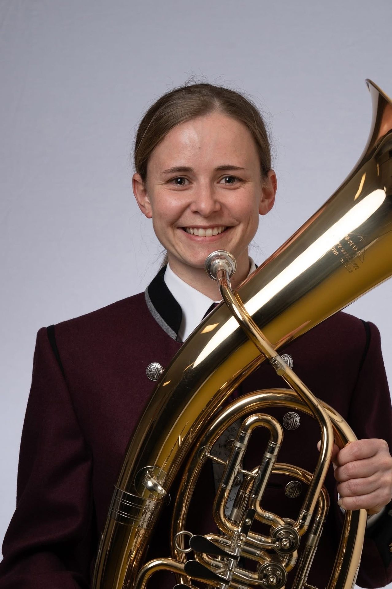 Eine Frau in Uniform mit einem Tuba, lächelt in die Kamera, wahrscheinlich in einem Fotostudio.
