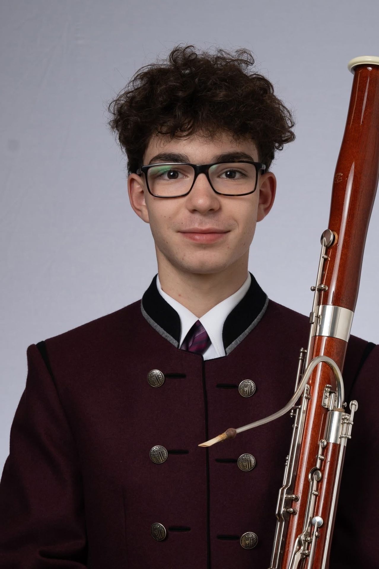 Ein junger Mann mit lockigem Haar lächelt und hält ein Fagott in einem Studio.
