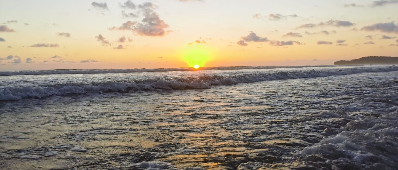 Die Sonne geht über dem Ozean unter und taucht die Wellen und den Horizont in ein goldenes Licht. Der Himmel ist in Rosa- und Orangetöne getaucht.