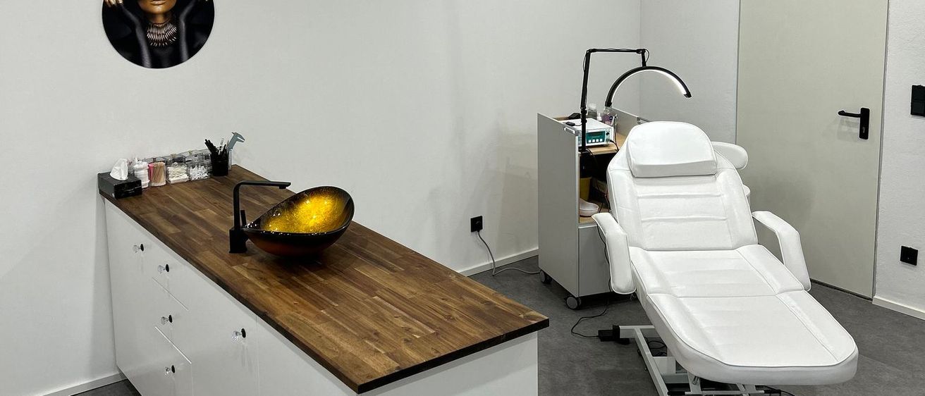 Ein minimalistischer ästhetischer Raum mit weißen Wänden, einer Holzdecke, einer Holzarbeitsplatte und einem weißen Liegestuhl. Eine beleuchtete Lampe und ein Porträt an der Wand.