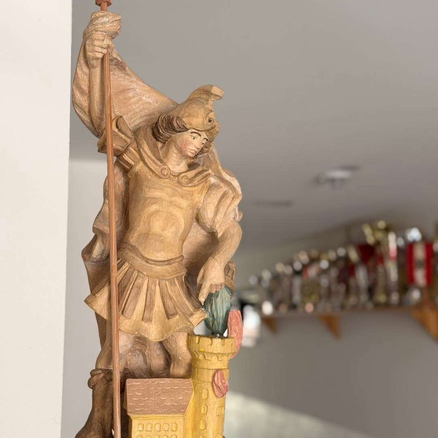 Eine Holzstatue eines Ritters mit einem Speer, einem Helm und einer Rüstung. Er steht auf einer Burg mit einem Turm und einer Flagge.