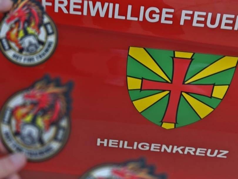 Ein roter Hintergrund mit einem weißen Text, der 'Freiwillige Feuer', ein rotes Kreuz auf einem grünen Schild und zwei weitere Embleme auf der linken Seite liest.