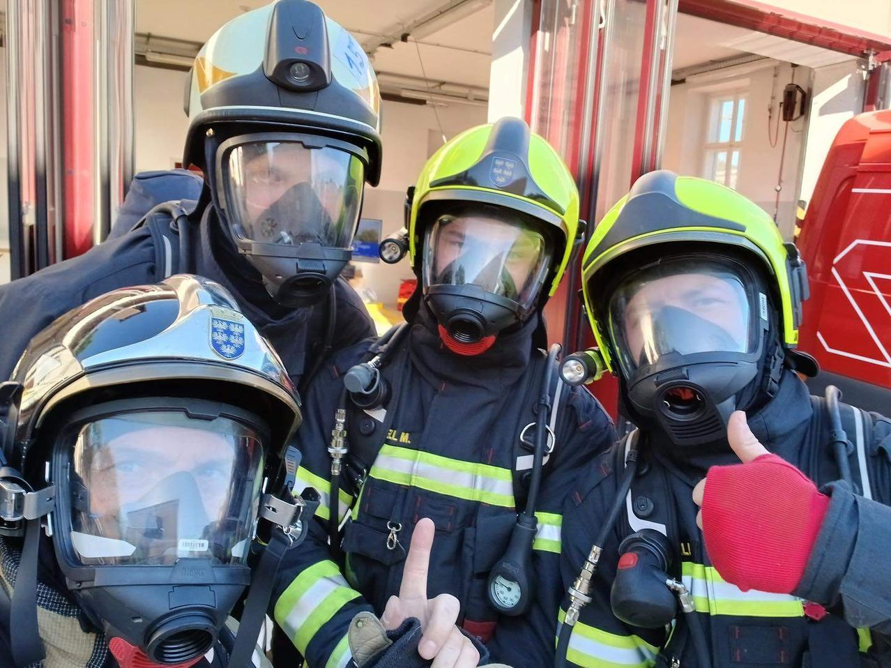 Eine Gruppe von Feuerwehrleuten in Schutzausrüstung mit Helmen steht in einer Feuerwache. Sie tragen Masken und posieren für ein Foto.
