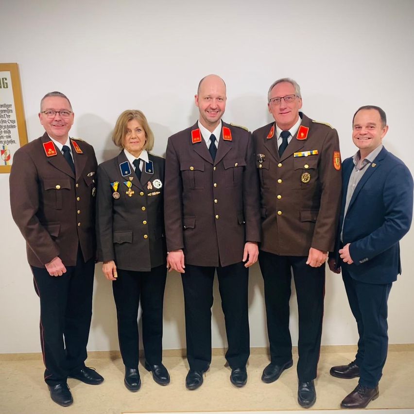 Fünf Personen, vier in Militäruniformen und eine im Anzug, stehen lächelnd zu einem Foto in einem Raum zusammen.