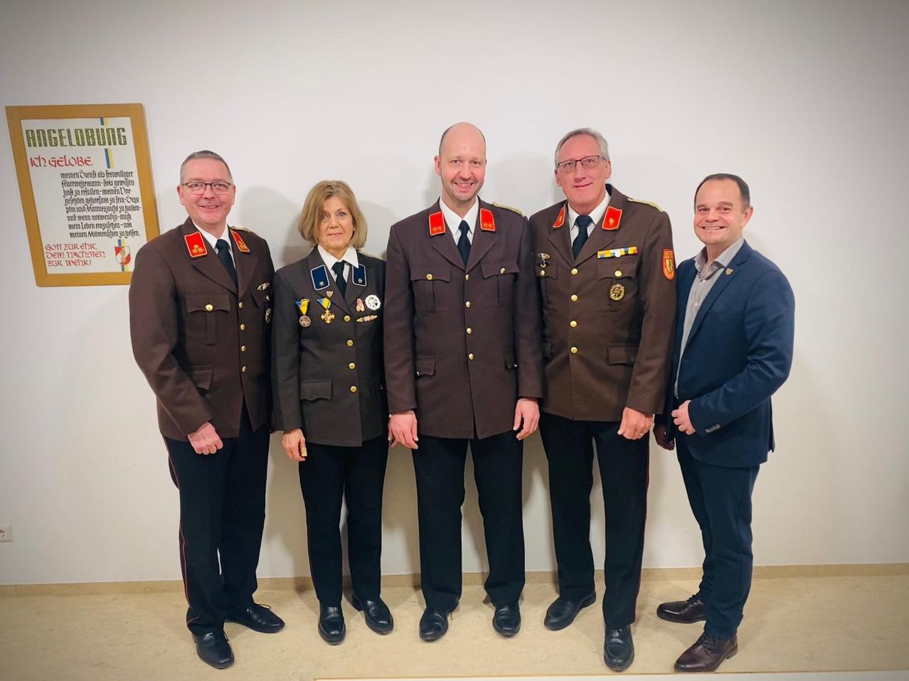 Fünf Personen, vier in Militäruniformen und eine im Anzug, stehen lächelnd zu einem Foto in einem Raum zusammen.