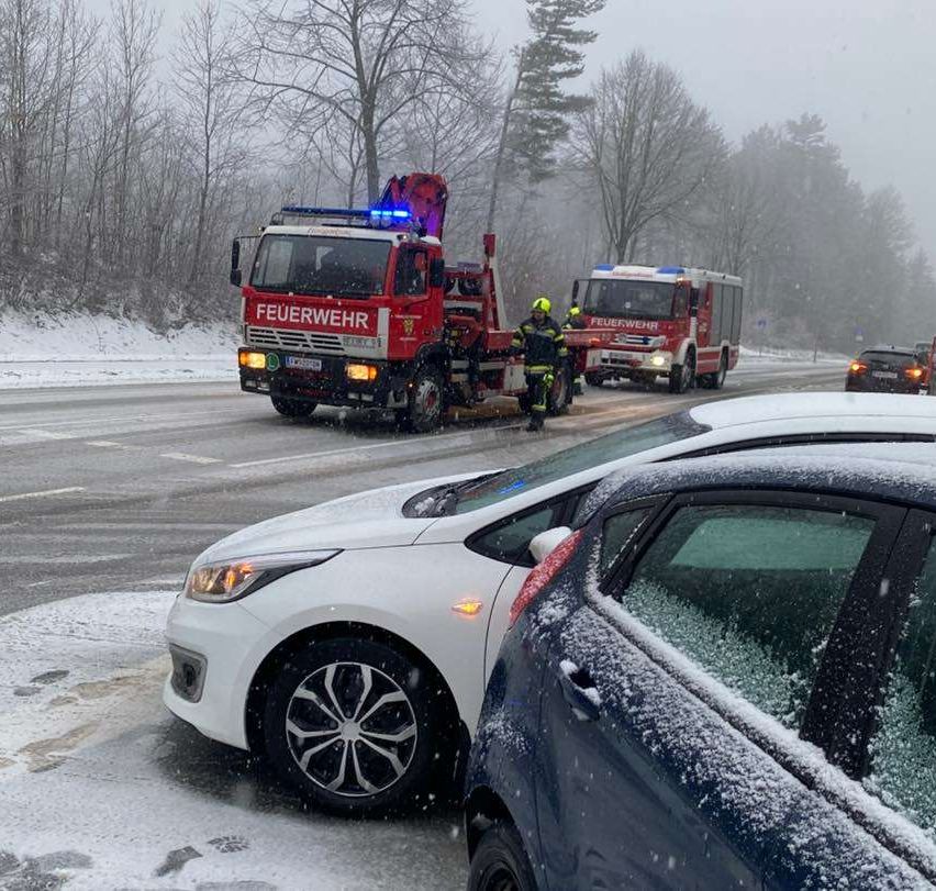 Rettungsfahrzeuge, darunter ein Feuerwehrwagen, sind auf einer verschneiten Straße, mit einer Person, die zwischen zwei Autos steht.