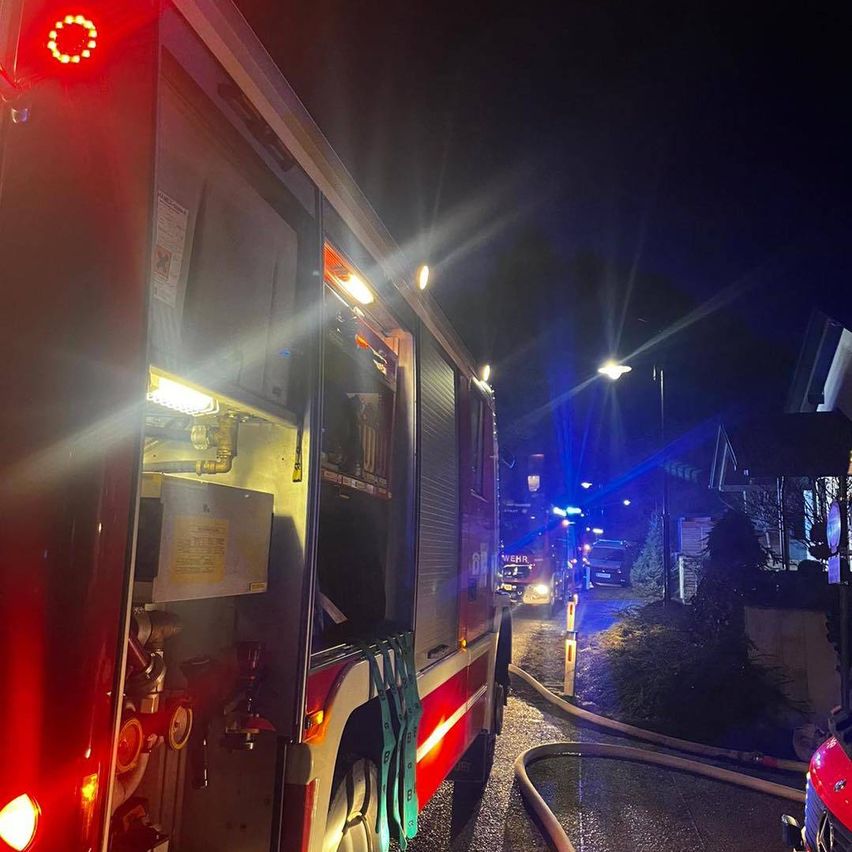 Ein Feuerwehrwagen mit eingeschalteten Lichtern steht bei Nacht auf einer Straße. Der Wagen hat rote Lichter auf der Rückseite und an den Seiten.