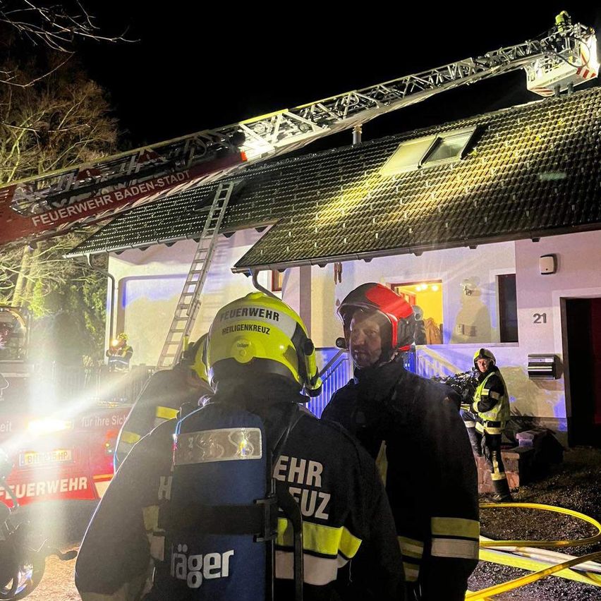 Feuerwehrleute aus Baden-Stadt sind nachts auf dem Dach eines Hauses und löschen einen Brand. Einige stehen auf einer Leiter.