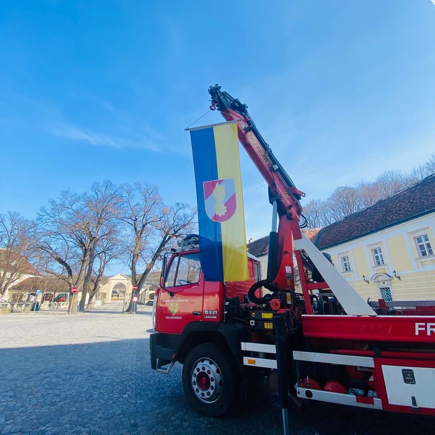 Ein roter Kran mit gehisster Flagge vor einem historischen Gebäude mit gelben Wänden unter einem klaren blauen Himmel.