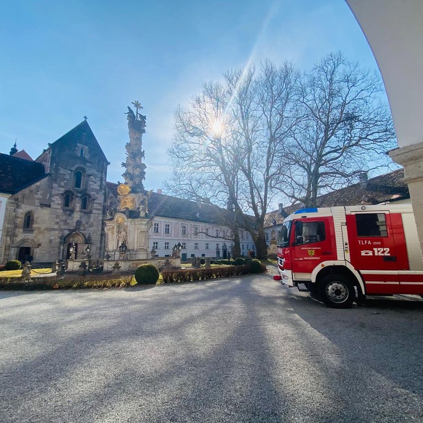 Ein Feuerwehrauto steht vor einem alten Gebäude mit einer großen Statue bei klarem Himmel.