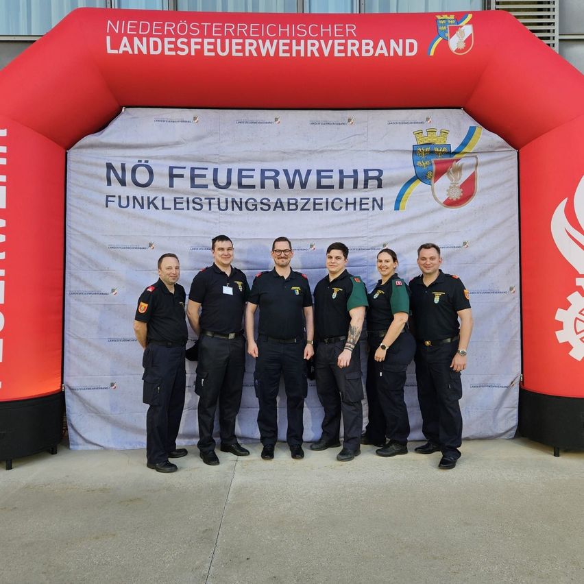 Sechs Feuerwehrleute in Uniform stehen vor einem Banner mit der Aufschrift 'Keine Feuerwehrsignale'. Dahinter befindet sich ein roter Bogen mit der Aufschrift 'Niederösterreichischer Feuerwehrverband'.